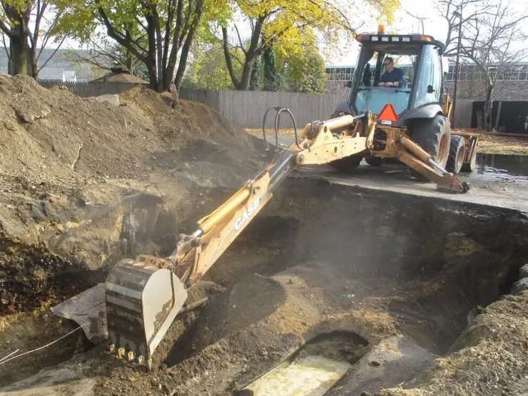 Case backhoe excavating a large open pit on a wooded lot in autumn