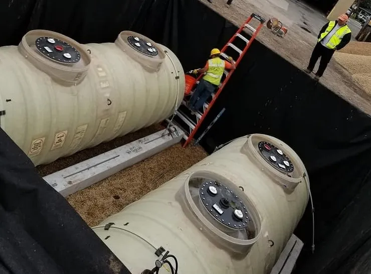Two new fiberglass underground tanks set in a gravel-lined pit with a worker on a ladder