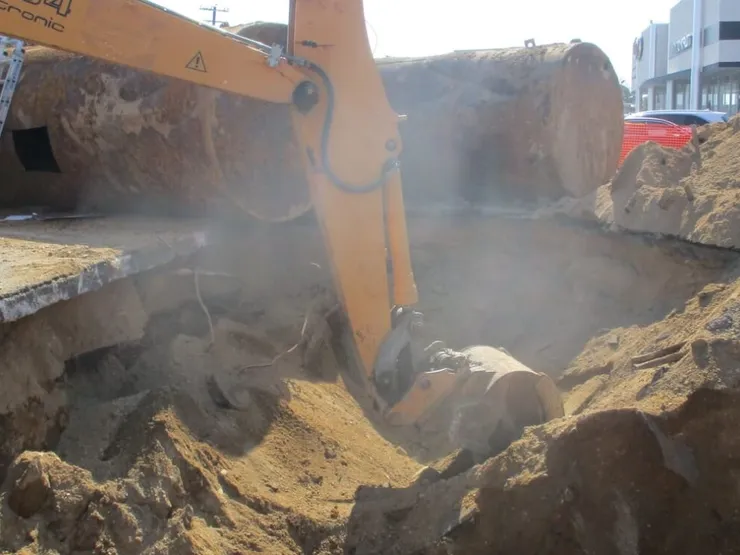 Excavator digging a sandy pit with removed rusty steel tanks lying alongside