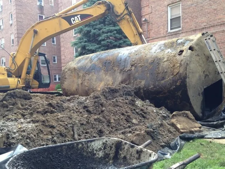 Rusty steel underground tank pulled from a pit beside a brick apartment building
