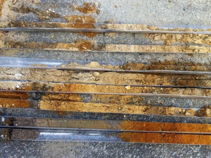 Layered soil cores in clear plastic sleeves laid on pavement showing tan and orange strata