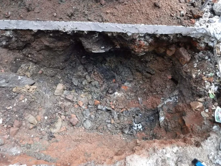 Close-up of petroleum-stained soil and brick rubble in an open excavation pit