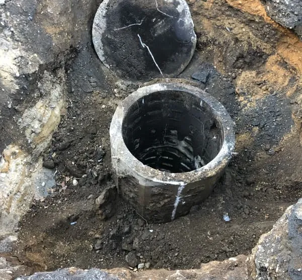 Exposed concrete drywell with its lid removed in an open excavation during closure
