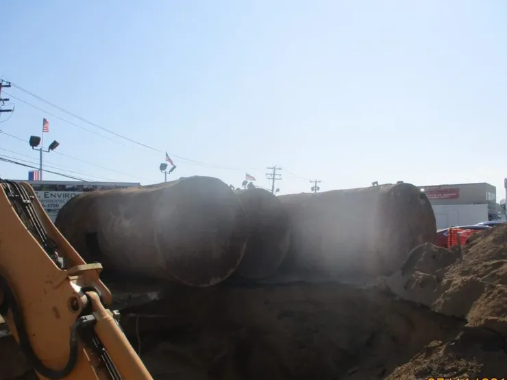 Two large rusty steel tanks beside an excavation with a GCE banner and flags