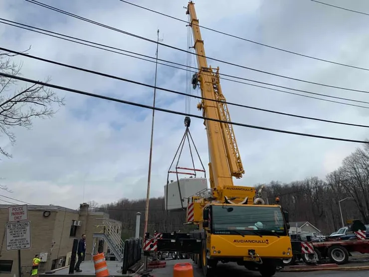 Mobile crane lowering equipment beside a police precinct under an overcast sky