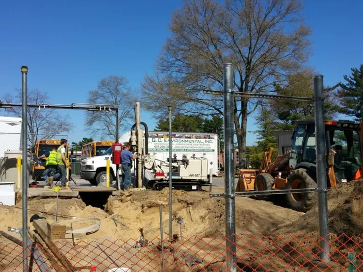 Worksite with a GCE truck, school buses, a drill rig, and a CASE backhoe