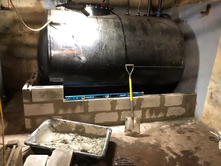 Black steel aboveground oil tank set on a new concrete-block containment base in a basement