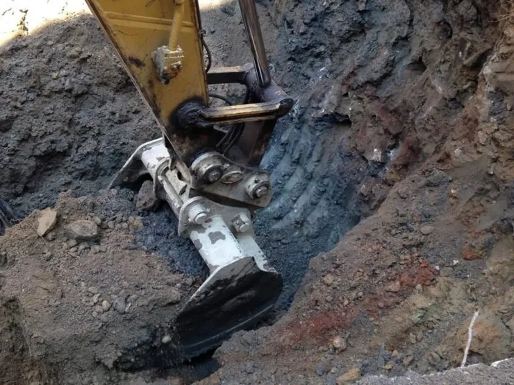 Excavator bucket digging black petroleum-stained soil from an open pit