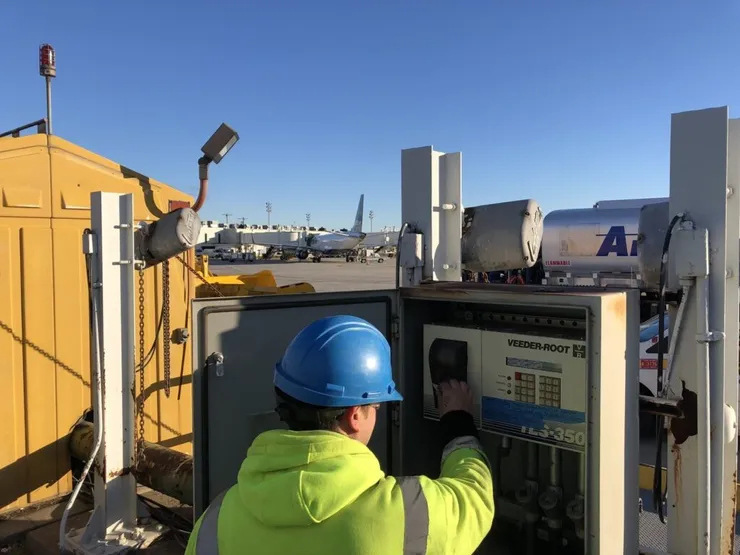 Worker operating a Veeder-Root TLS-350 tank gauge console on an airport tarmac