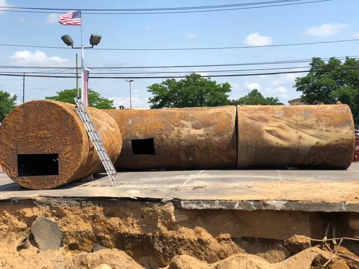 Three removed rusty steel tanks with cut access holes in a dealership parking lot