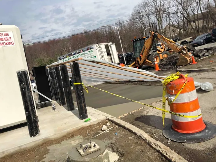 Fresh concrete tank pad with a GCE truck, backhoe, and caution-taped traffic barrel