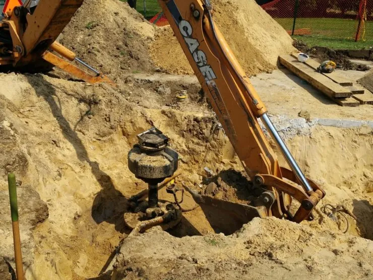 CASE backhoe excavating a sandy pit to expose an underground tank sump riser