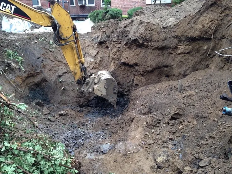 CAT excavator removing dark contaminated soil from a deep excavation