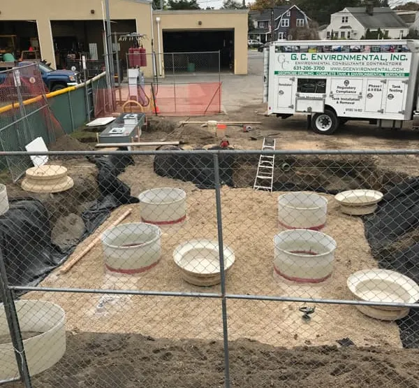 Capped tank sump risers in fresh backfill with a GCE equipment trailer behind a fence