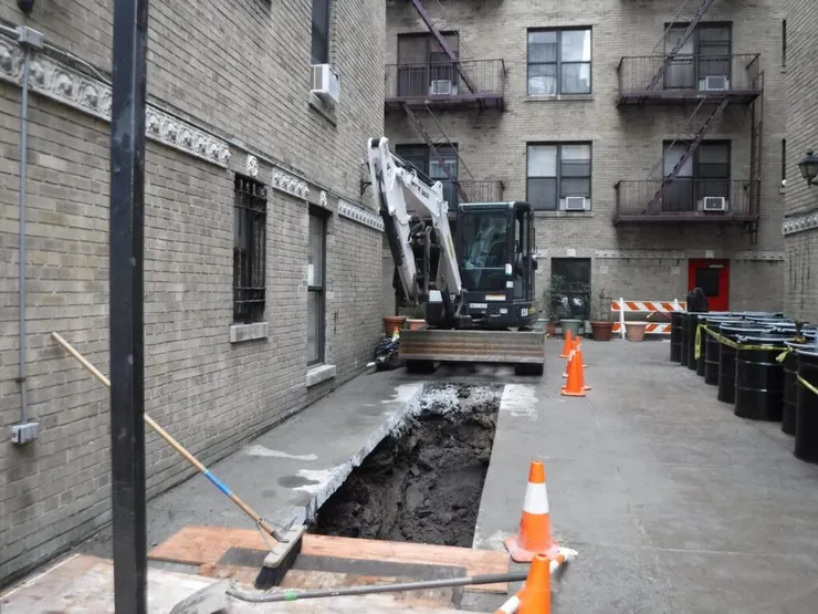 Compact excavator digging a trench in a brick apartment courtyard with traffic cones