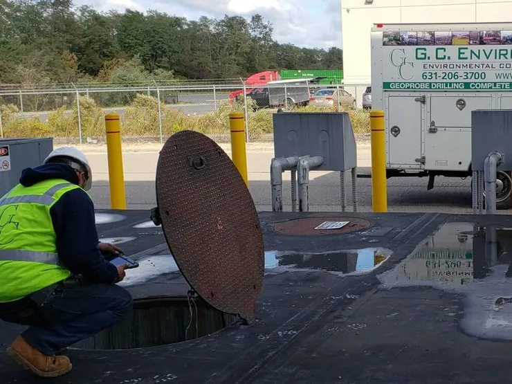 GCE worker in a hi-vis vest checking an open steel tank lid beside a GCE box truck