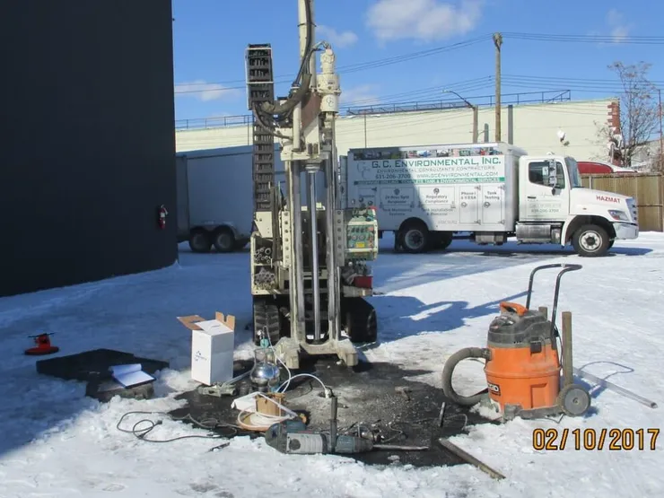 Track-mounted Geoprobe rig drilling a soil boring on a snowy lot beside a GCE box truck