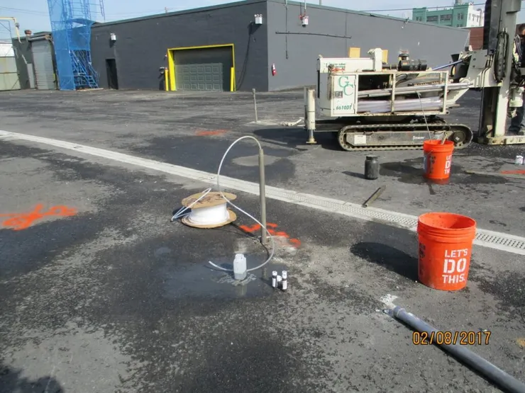 Geoprobe rig and a groundwater sampling point on a paved lot marked with utility paint